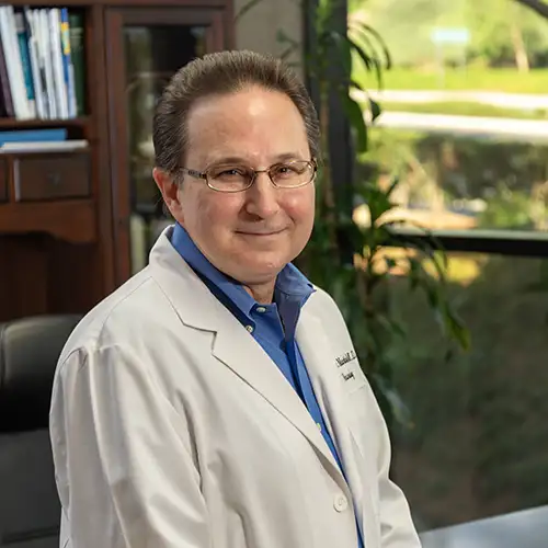 Head and shoulders portrait of Dr. Kenneth P Martinez wearing a labcoat and sitting in his office