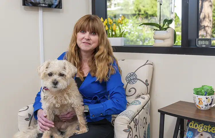 Allison Smith, sits on a floral upholstered chair with her dog in her lap.
