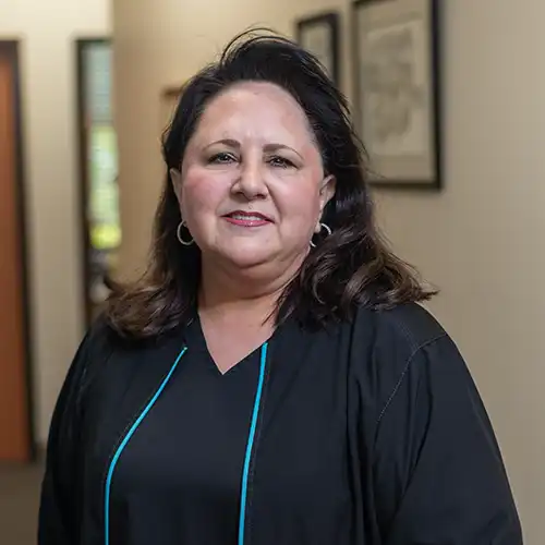 A woman with shoulder-length dark hair wears black scrubs and a black jacket. She smiles at the camera