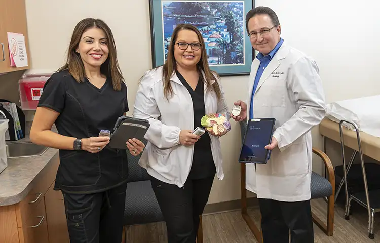 Dr. Martinez poses with Vanessa Madrigal and Rebekah Torres, holding a DBS device and a brain sculpture for demonstration.