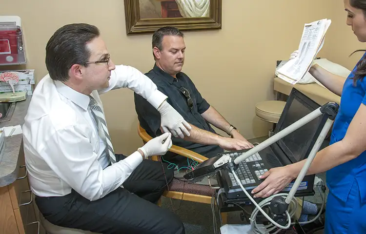 Dr. Kenneth Martinez, dressed in a long-sleeved dress shirt and tie, tests a patient for focal spasticity treatments
