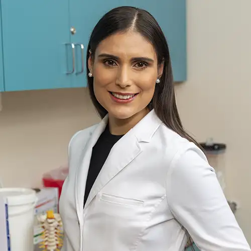 Elizabeth Rodriguez looks over her left shoulder and smiles at the camera. She wears a white lab coat.