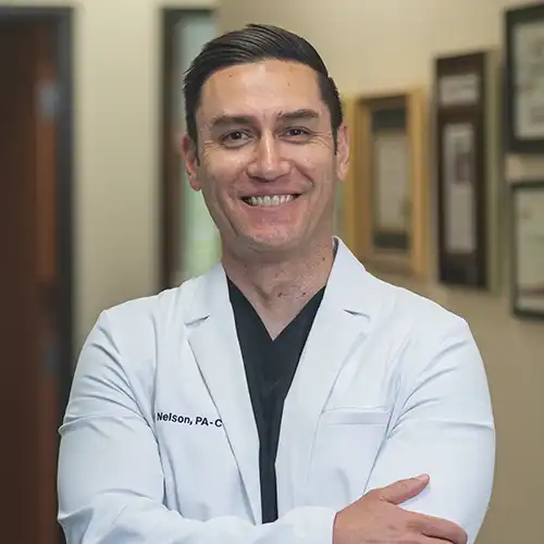 Male doctor in a white lab coat stands with his arms crossed and smiles at the camera