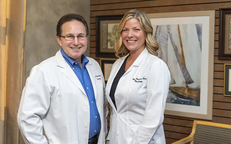 Dr. Kenneth Martinez and Wendy Reulman post in the lobby of the headache clinic. A painting and drapes are visible in the background.