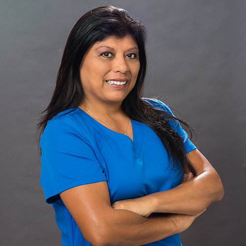 Irene Ybarra poses with her arms crossed. She wears blue scrubs.