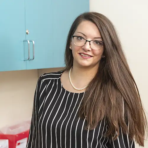 Juliana Stoilova looks at the camera and smiles. She is wearing a black blouse with white stripes and a pearl necklace.
