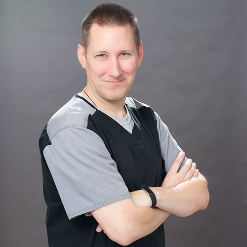 Michael Husava stands with his arms crossed, turned at a three-quarter angle, smiling.