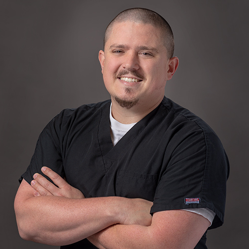 Robert Weldy poses in black scrubs with his arms crossed.