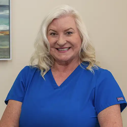 Tracey Bennet poses in her exam room wearing blue scrubs
