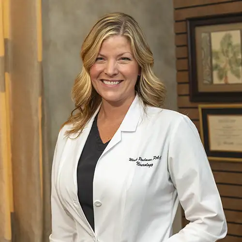 Wendy Reulman stands in the lobby of the headache clinic. She wears a white lab coat and smiles at the camera.