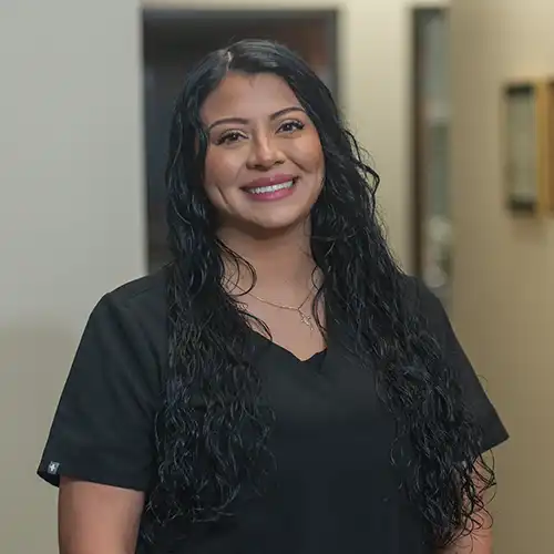 Woman with long dark hair in black scrubs smiles at the camera
